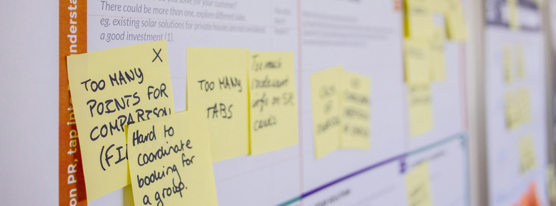 Close-up of a project planning board with multiple yellow sticky notes detailing user feedback, including phrases like 'Too many tabs' and 'Hard to coordinate booking for a group' — representing agile backlog refinement or UX issue identification