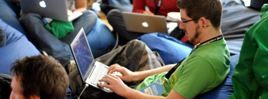 A group of young developers collaborating in a relaxed setting, seated on bean bags with laptops, engaged in coding and problem-solving during a tech-focused event or hackathon.