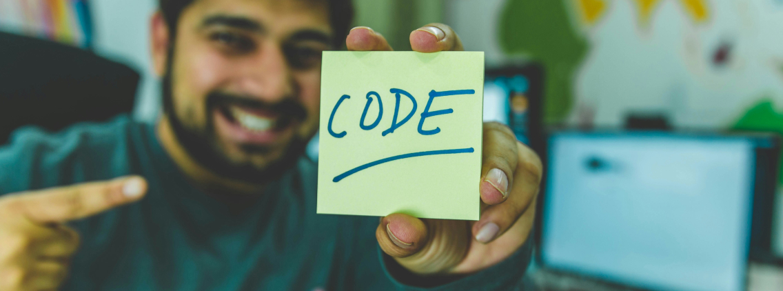 Smiling developer holding a sticky note with the word 'CODE' written on it, emphasizing enthusiasm and passion for programming