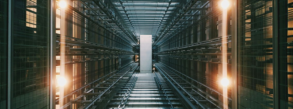 Symmetrical view of a futuristic, metallic interior resembling a data center or elevator shaft, illuminated by warm golden lights. The reflective surfaces and structured lines create a sense of depth and scale