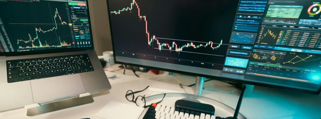 Dual-monitor workstation displaying data analytics dashboards and real-time stock market graphs, set in a modern office environment
